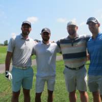 Four football alums posing for a photo together on the golf course.